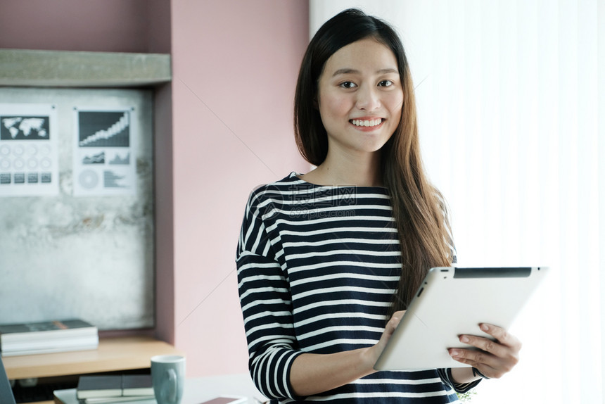 电脑药片年轻的亚洲女商人在办公室临时生活概念中使用有微笑脸的平板正面情绪和积极的平板图片