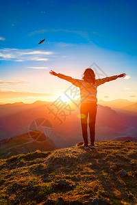 鸟飞日落时山顶上的女人看着老鹰张开双臂登山者图片
