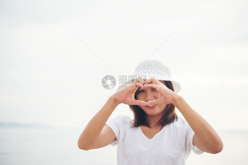 女快乐的年轻子在海滩上玩耍度假时做一个心脏形状放松旅行图片
