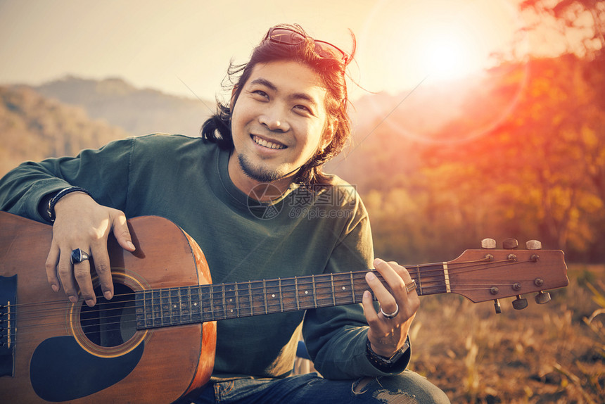 以快乐的笑脸微着幸福的亚洲人弹吉他和日落的天空背景露齿爱好潮人图片