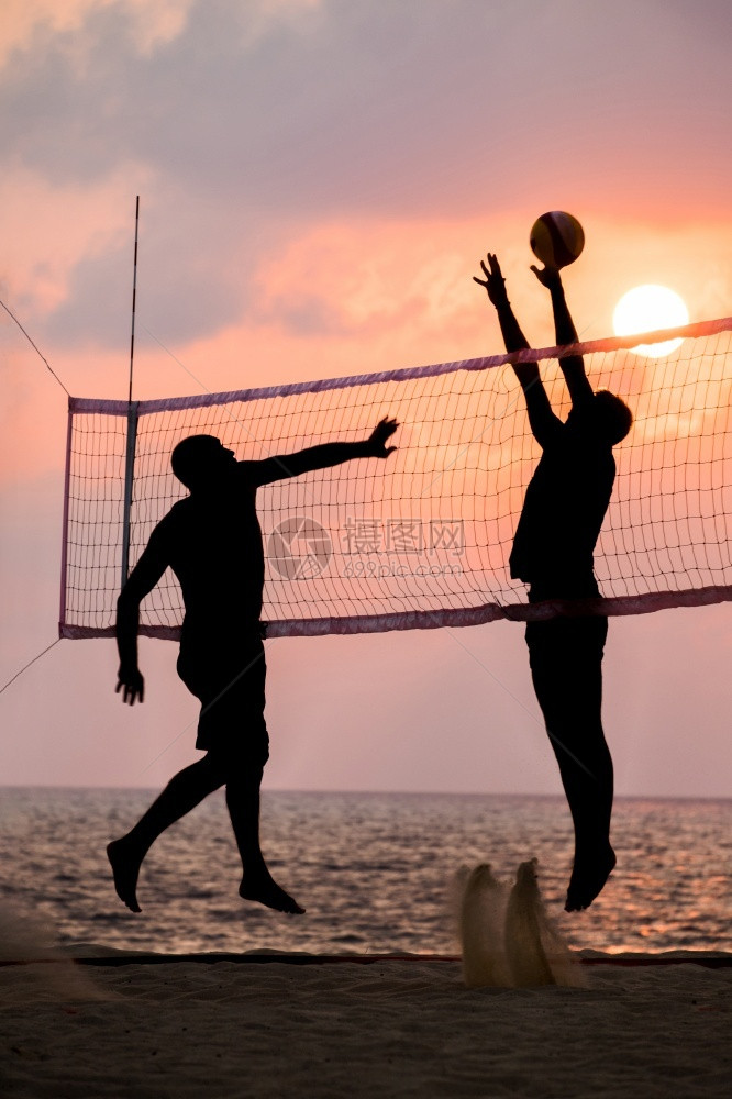 夕阳下在沙滩边打排球的人们图片