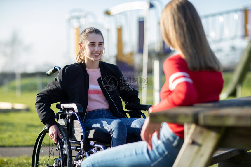决心乐趣女孩在轮椅上与朋友公园交谈坐着图片