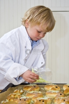 洒水器一个男孩穿着厨师皮夹克撒洒在甜面包上浓度的图片