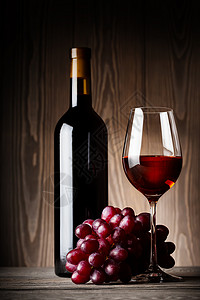 香槟酒黑瓶和一杯红酒配木背景的葡萄黑瓶和一杯红酒配葡萄玫瑰图片