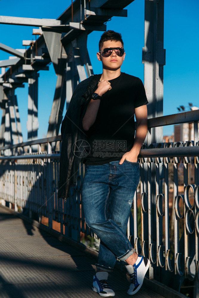 城市的随意时尚带着太阳眼镜的年轻人在金属桥上行走图片