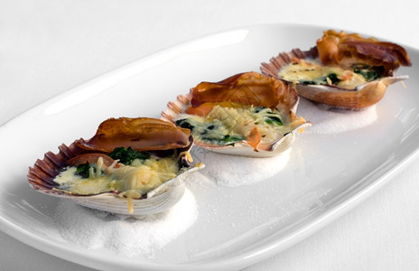 晚餐贝类壳中的塔斯马尼亚扇贝与潘塞塔菠菜和两奶酪酱一起烤可口图片