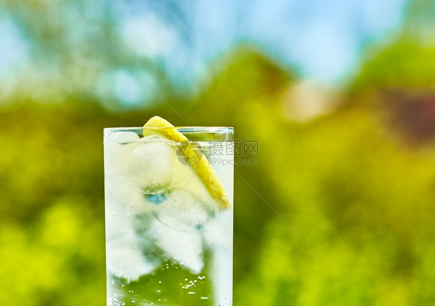 夏天的阳光明媚一天在玻璃上加冰的闪光水和柠檬片狭窄地聚焦于玻璃中间绿色新鲜图片