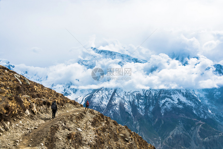健康徒步旅行跋涉两名游客在喜马拉雅山上沿着岩石道行走尼泊尔云中雪峰高山图片