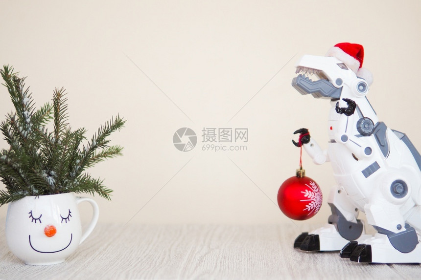 圣诞节冷杉一种玩具机器人恐龙在圣诞老人帽子与一个fir球和雪人杯与fir树枝在米色背景复制空间图片