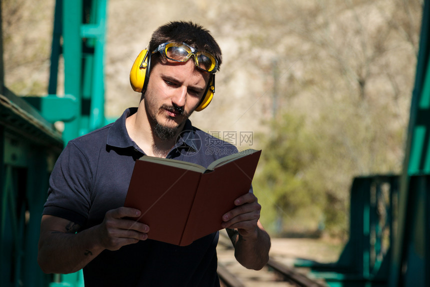 在职的白天阅读年轻建筑工人在读一本关于旧钢铁路桥的书时图片