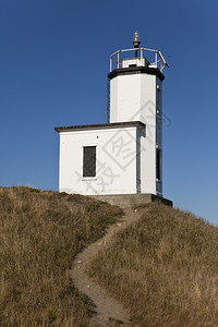 白色的爬坡道栏杆圣胡安岛的牛港灯塔在一条通向山顶的风尘道尽头图片