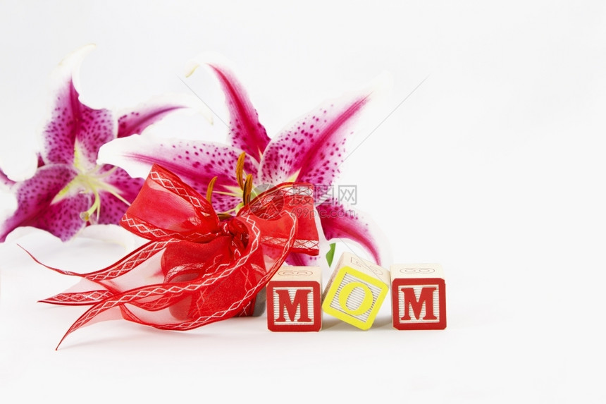 粉色的天上面写着MOM的字母区块在一件红丝带包着的礼物和两件独百合花前全都放在白色背景上单身的图片