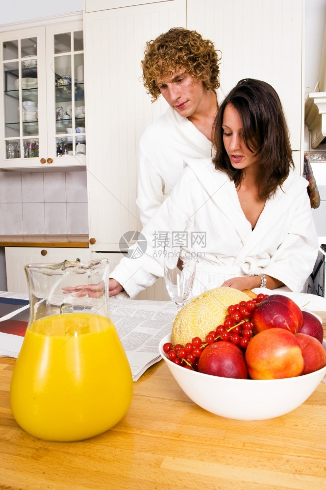 年轻一对在享受美食时看报纸的年轻夫妇穿着浴袍吃愈合的早餐健康法水果图片