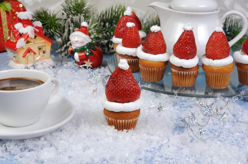 在松饼上戴圣诞帽子配奶油的草莓和鲜新箔晚餐图片
