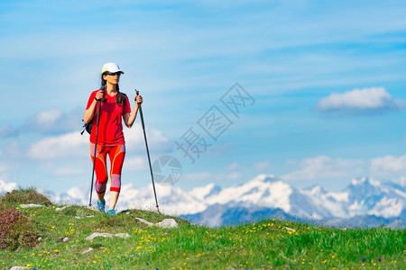 身着红色和高山的红色旅游服装在前滩绿草上漫雪的妇女远足冒险天空图片