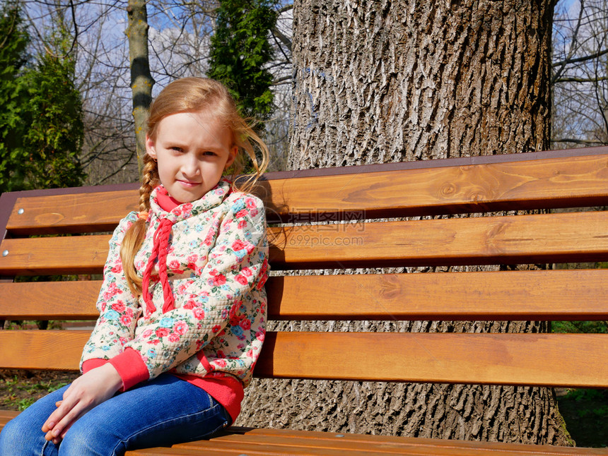 棕色的颜小美丽高加索女孩在春天坐公园的木板凳上坐在公园里木制的图片