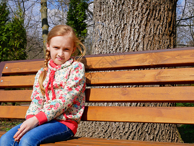 棕色的颜小美丽高加索女孩在春天坐公园的木板凳上坐在公园里木制的图片