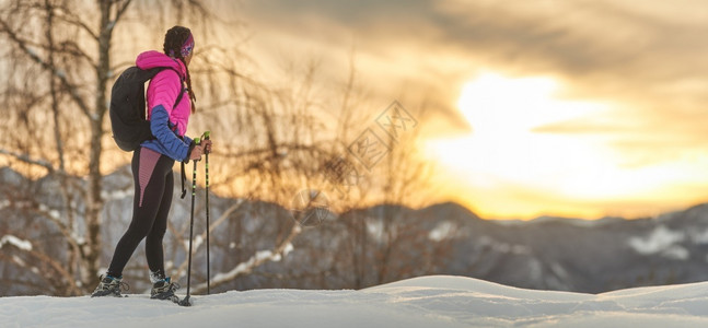 冒险一个运动女孩在雪鞋上漫步时看着日落走女士图片