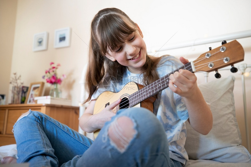 享受女孩学习玩Ukulele坐在床上睡觉有创造力的家图片