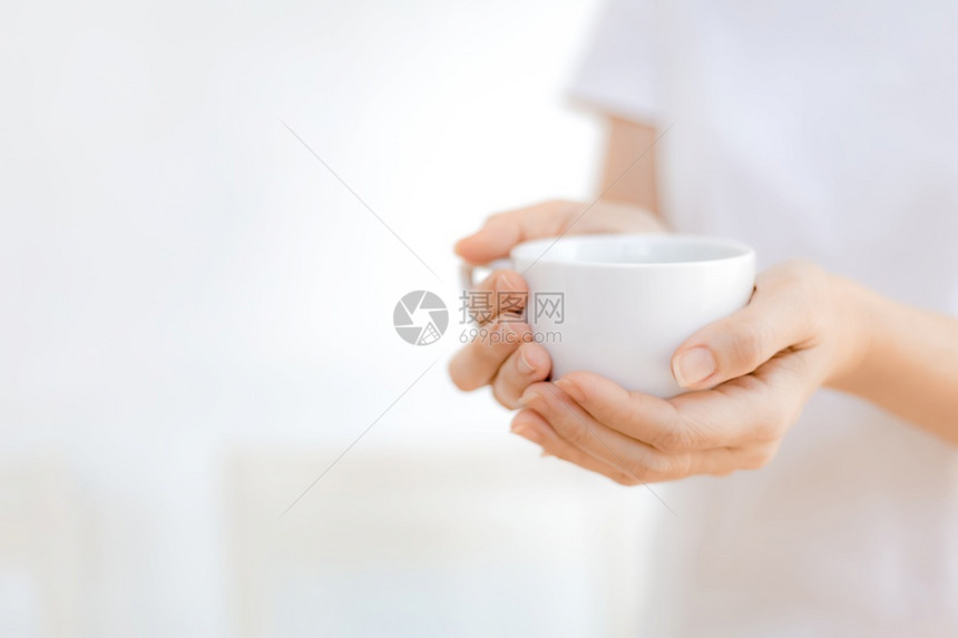 手指陶瓷制品妇女用手在清晨光照亮的白背景上拿着色热咖啡杯因图片