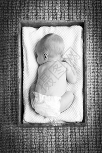 新生婴儿睡在古老的木板箱中用美丽的黑白布和色黑睡觉图片
