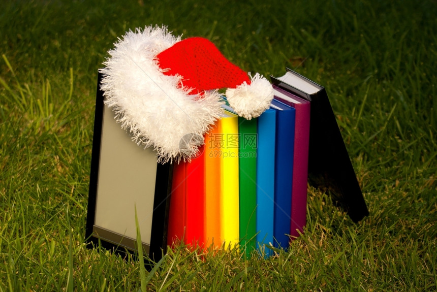 电子图书阅读器佩戴Santarsquos帽子和一排书籍小说草电子阅读图片