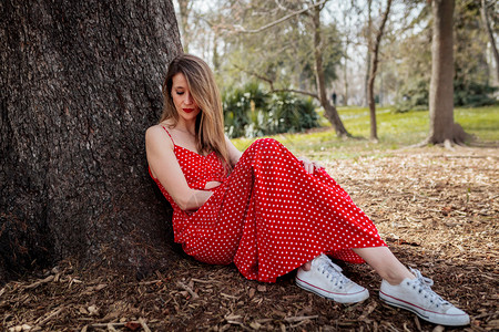 身着红长裙坐在树旁的金发年轻女郎热的长自然图片