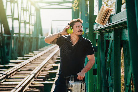 一种保护火车年轻建筑工人在读一本关于旧钢铁路桥的书时手里拿着液压锤子图片