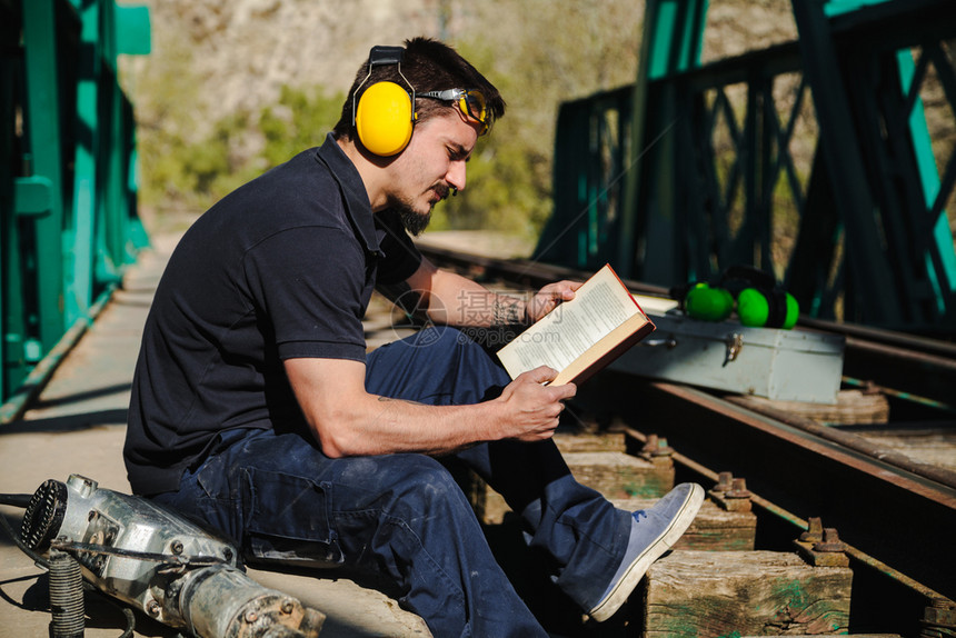 胡子年轻建筑工人在读一本关于旧钢铁路桥的书时白天梁图片