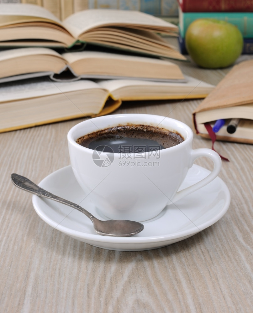桌子上一杯咖啡背景是一本开着的书上面有一本笔记和堆书食物知识碟子图片