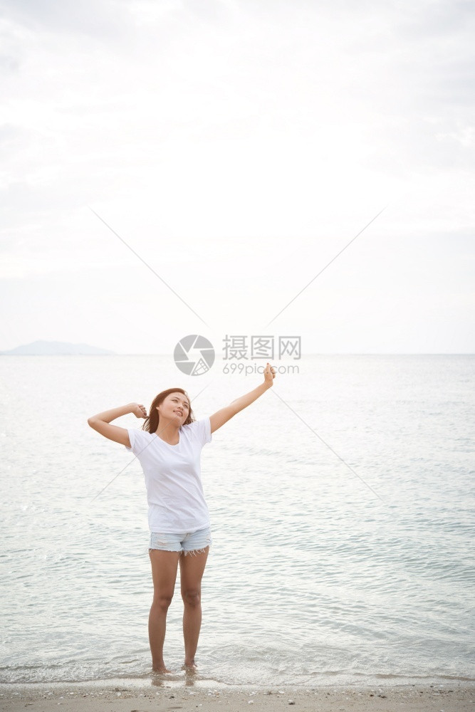 年轻美女站在海滩上赤脚放轻松的节日中举起双臂在空中伸展水女拉紧图片