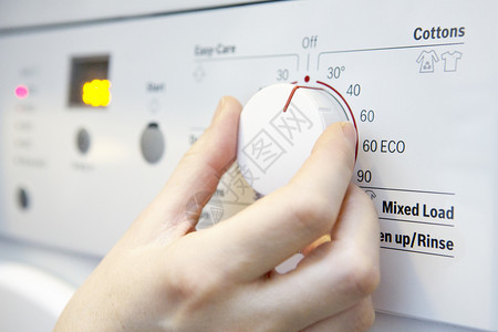 妇女为节省能源而在洗衣机上选择更冷却的温度服装控制寒冷的图片