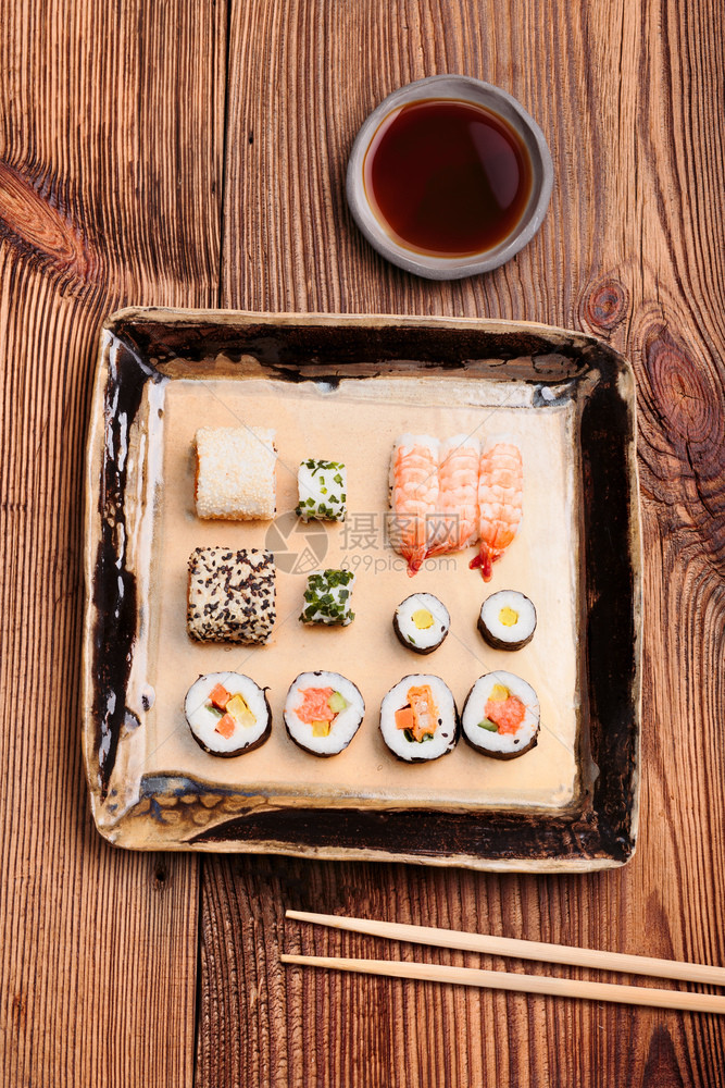 木头新鲜的把寿司放在瓷器板上面的旧木制餐桌上碗里有筷子和酱油美食图片