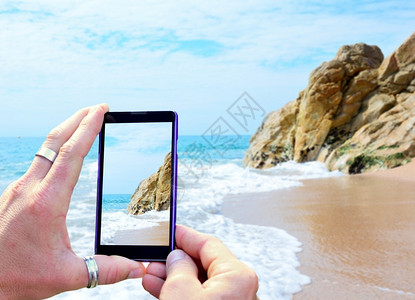用手机拍摄海滩的手部特写图片
