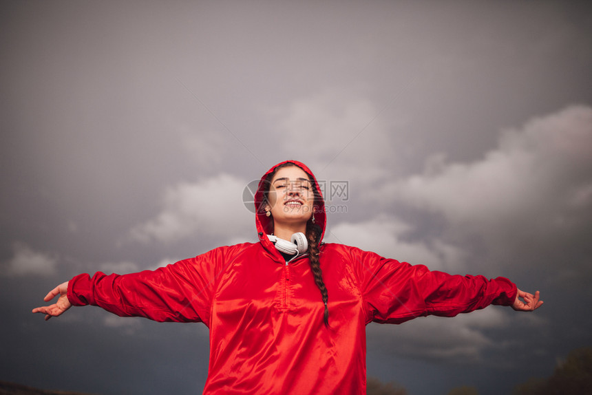 下雨年轻女子在天与衣和耳机一起站在田地上放松红色的图片