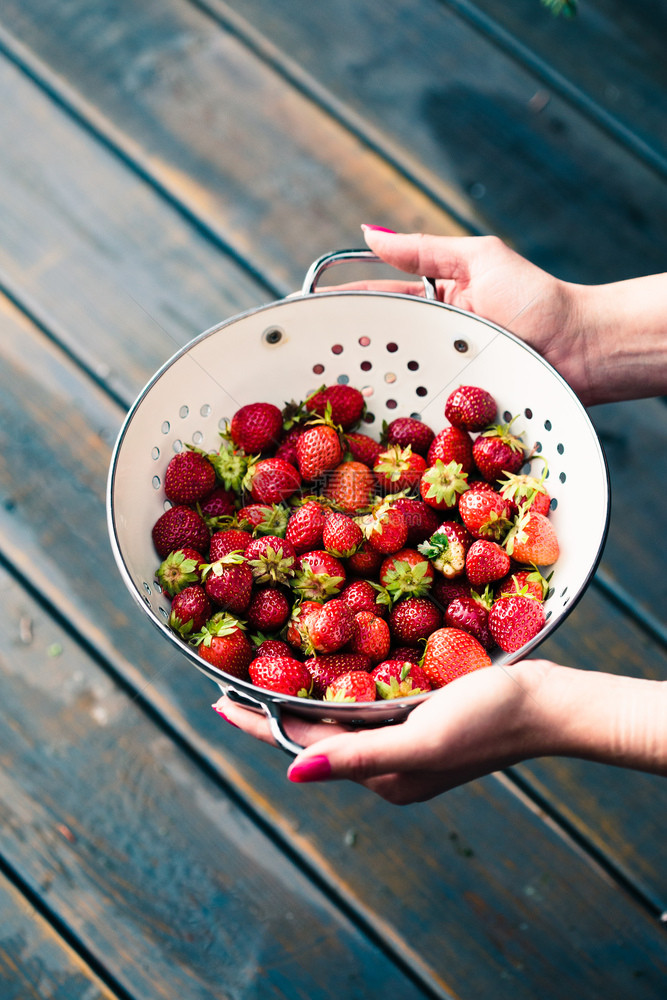 生的自然素食主义者女手握着一碗新鲜草莓在木桌上洒下雨滴图片