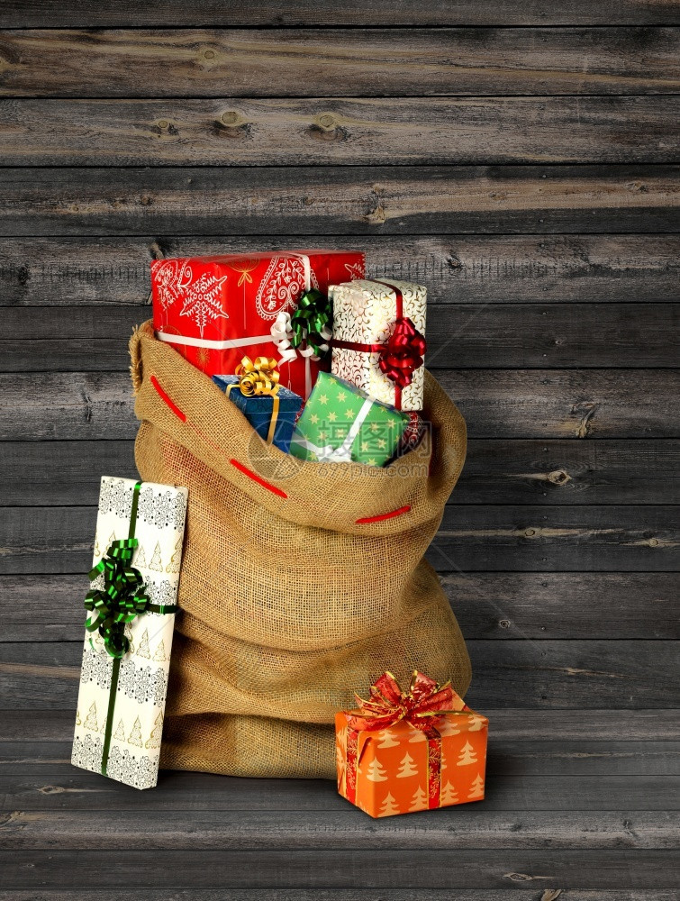 假期满的圣誕老人现口袋和礼品箱用旧的灰色木板墙姜饼小屋和圣诞树棕色的图片