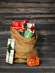 假期满的圣誕老人现口袋和礼品箱用旧的灰色木板墙姜饼小屋和圣诞树棕色的图片