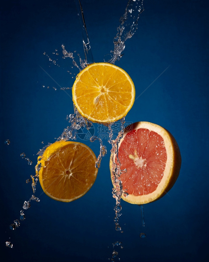新鲜在深蓝背景上喷水的橙子和葡萄园切片悬浮成像创意合图象蓝色的多汁图片