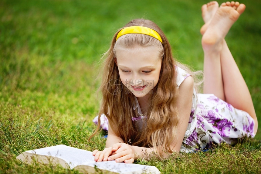 可爱的9岁女孩躺在绿色草地前线阅读一本书金发户外随意的图片
