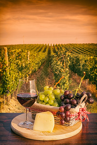 束一杯红葡萄酒篮子里的葡萄和芝士在日落的葡萄园前黄夕的葡萄园前一种簇图片