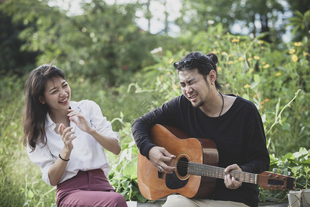 更年轻声学笑青的亚洲男女玩吉他和快乐感弹背景图片