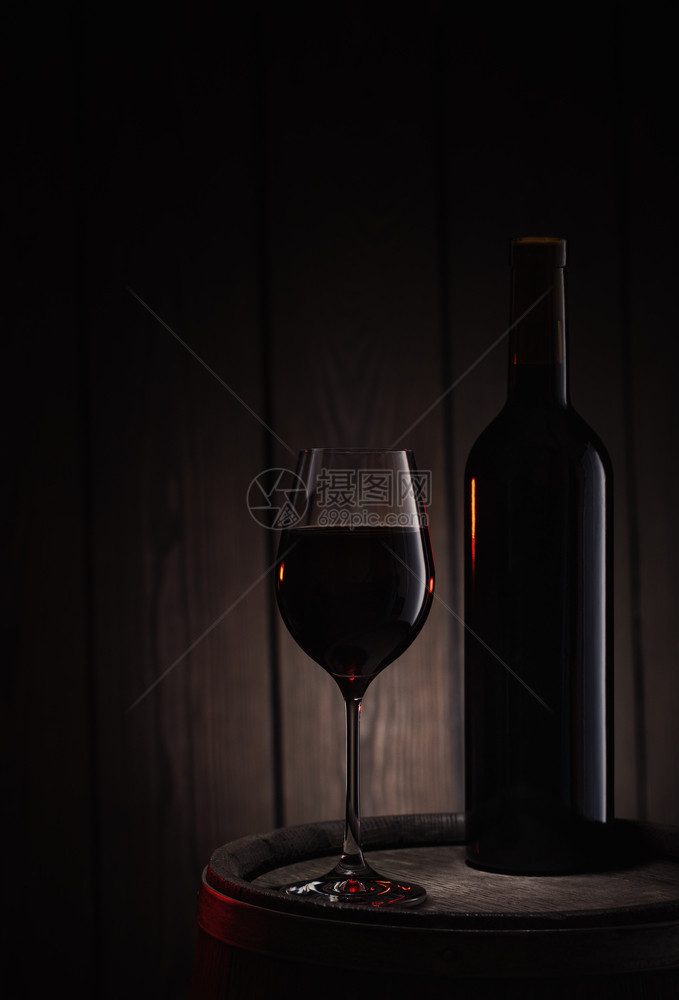 派对酒瓶和一杯红摊在旧木桶上背景的棍子瓶和杯红酒摊在旧木桶上玻璃器皿优雅的图片