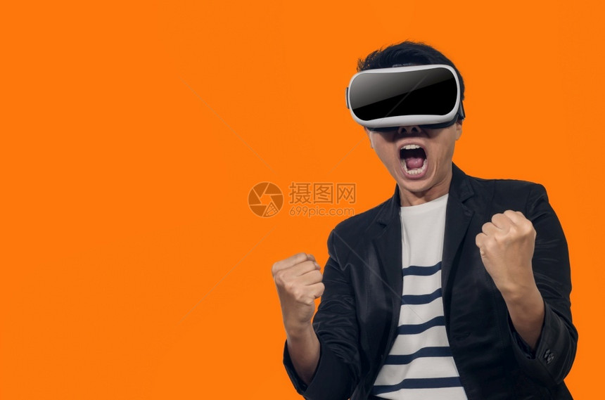 有虚拟现实头盔的年轻人站在橙色背景的室内青年拿着虚拟现实头盔的年轻人乐趣游戏玩图片