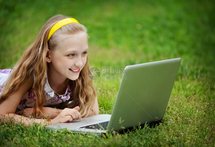 可爱的9岁女孩在绿色草地前边躺着看笔记本电脑学习随意的图片