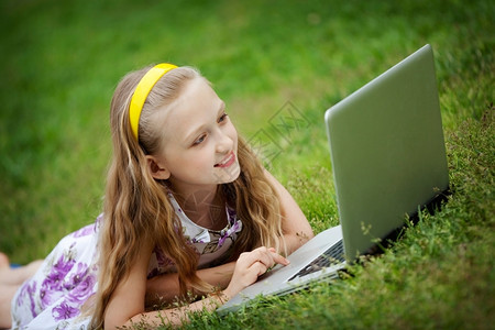 9岁女孩在绿色草地前边躺着看笔记本电脑水平的童年学习图片