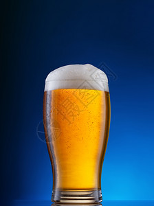 玻璃杯蓝色背景上放轻啤酒蓝色背景上放轻啤酒棕色的满贮藏啤酒图片