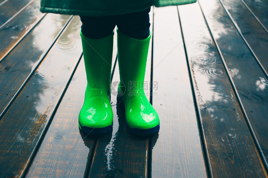 常设天气身着绿色油井和雨衣穿着亮绿色的雨靴子站在门廊上立的小孩腿紧闭水图片