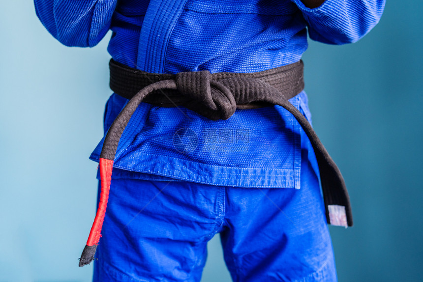 紧贴在墙前身着蓝色和服的运动员拳手腰部上方的Bjjbrazilianjiujitsu黑带中间战斗姿态大约图片