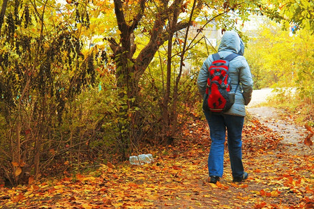 女士秋天带着包从森林向城镇出口的年轻女子图片